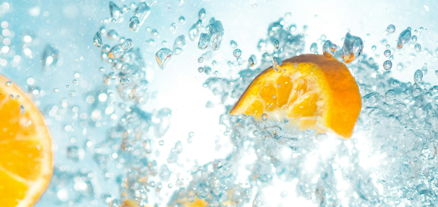 Orange slices floating in clear sparkling water with bubbles and droplets, photographed in a bright studio-style close-up to promote Wavee Water. 